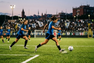 Calciatrici in campo in una partita serale di calcio femminile sotto le luci dello stadio