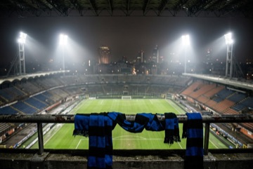 Lo stadio di San Siro di notte visto dalle tribune, fari accesi e sciarpe nerazzurre in primo piano