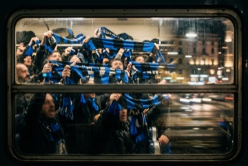 Tifosi nerazzurri in viaggio verso una partita in trasferta, sciarpe blu e nere al finestrino di un treno di sera