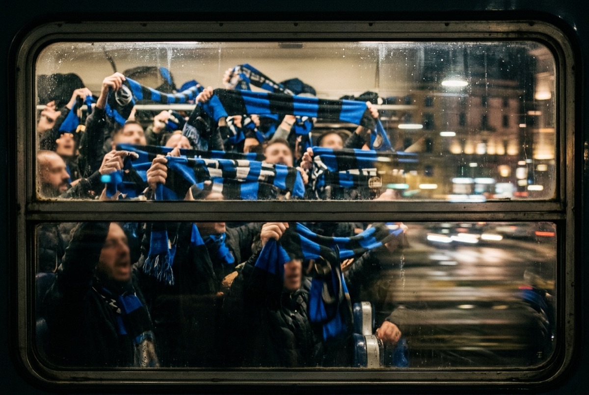 Tifosi nerazzurri in viaggio verso una partita in trasferta, sciarpe blu e nere al finestrino di un treno di sera